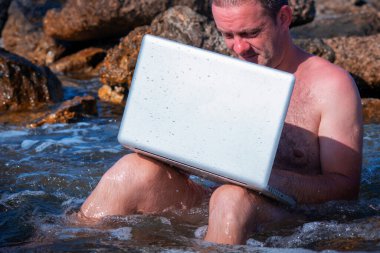 Her yerde ve her zaman çalışıyor. Deniz taşları üzerinde dizüstü bilgisayarla çalışan bir iş adamı.. 