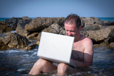 Her yerde ve her zaman çalışıyor. Deniz taşlarında dizüstü bilgisayarla çalışan bir iş adamı.. 