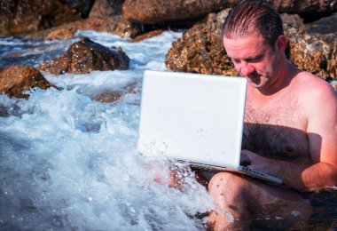 Her yerde ve her zaman çalışıyor. Deniz taşlarının üzerinde dizüstü bilgisayarla çalışan bir iş adamının portresi. Yatay görüntü. Boşluğu kopyala.
