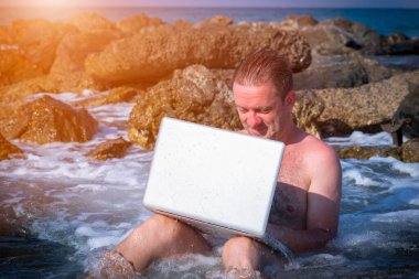 Her yerde ve her zaman çalışıyor. Deniz taşları üzerinde dizüstü bilgisayarla çalışan bir iş adamının portresi. Yatay resim.