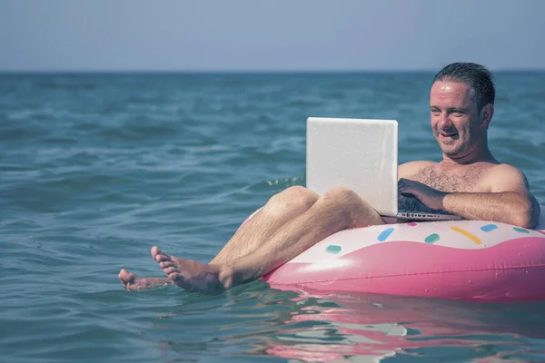 Adam denizdeki bir dizüstü bilgisayarda çalışıyor. Eğlence ve uzaktan çalışma konsepti. Boşluğu kopyala.