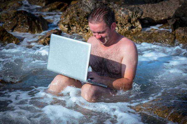 Her yerde ve her zaman çalışıyor. Deniz taşlarının üzerinde dizüstü bilgisayarla çalışan işadamının komik bir görüntüsü..