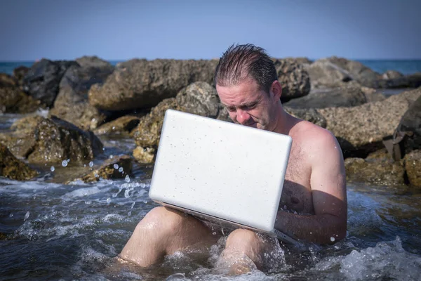 Her yerde ve her zaman çalışıyor. Deniz taşlarının üzerinde dizüstü bilgisayarla çalışan bir iş adamının komik portresi..
