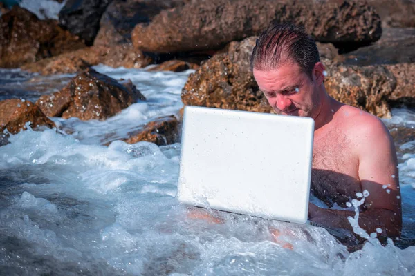 Her yerde ve her zaman çalışıyor. Deniz taşlarının üzerinde dizüstü bilgisayarla çalışan bir iş adamının portresi. Boşluğu kopyala.