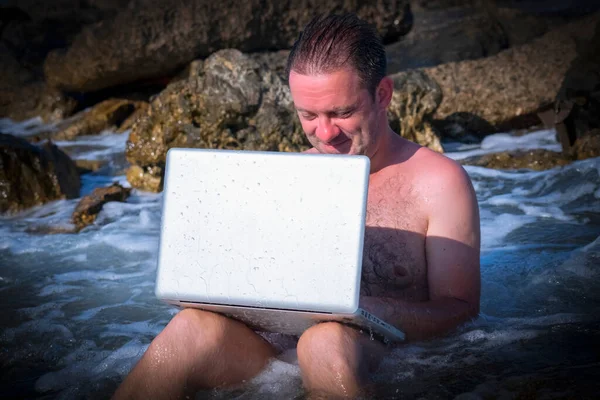 Her yerde ve her zaman çalışıyor. Deniz taşları üzerinde dizüstü bilgisayarla çalışan bir iş adamının portresi.