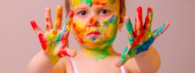 Çocuk makyajının komik bir görüntüsü. Güzellik, moda, mutlu çocukluk kavramı. Yüzü ve elleri boyalı güzel bir kızın portresi. Ellere seçici odaklanma.