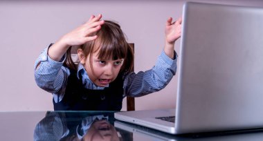 Çocuklar için çevrimiçi eğitim. Çok kızgın bir kız çocuğu dizüstü bilgisayarla uzaktan öğreniyor. Yatay resim.