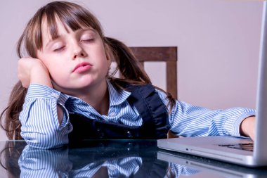 Çocukların fiziksel ve zihinsel sağlıklarında günlük hayatta dijital cihazların aşırı kullanımı tehlikesi. Bitkin, yorgun ve uykulu genç kız dizüstü bilgisayarın önünde oturuyor. 