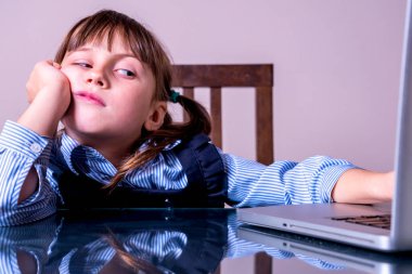 Çocuk konsepti için online eğitim. Dizüstü bilgisayarın önünde oturan çok sıkılmış küçük tatlı bir kızın portresi. Yatay resim.