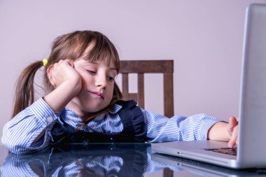 Çocuk konsepti için online eğitim. Dizüstü bilgisayarın önünde oturan çok sıkılmış küçük tatlı bir kız çocuğu. Yatay resim.