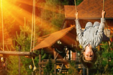 Genç ve güzel bir kız baş aşağı asılı ve dışarıda salıncakta eğleniyor. Mutlu çocukluk, yaz tatili, tatil ve dinlenme konsepti.