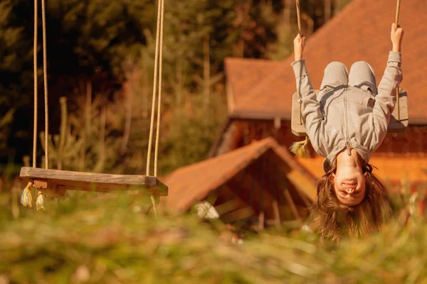 Genç ve güzel bir kız baş aşağı asılı ve dışarıda salıncakta eğleniyor. Mutlu çocukluk, yaz tatili, tatil ve dinlenme konsepti. Tasarım için alanı kopyala.