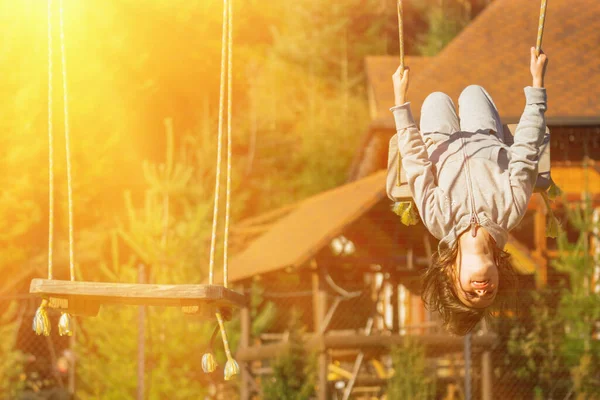 Genç ve güzel bir kız baş aşağı asılı ve dışarıda salıncakta eğleniyor. Mutlu çocukluk, yaz tatili, tatil ve dinlenme konsepti. Yatay görüntü. Boşluğu kopyala