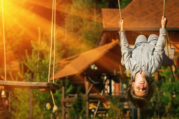 Genç ve güzel bir kız baş aşağı asılı ve dışarıda salıncakta eğleniyor. Mutlu çocukluk, yaz tatili, tatil ve dinlenme konsepti.