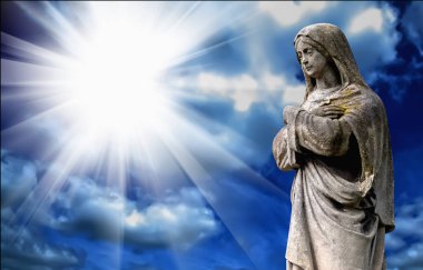 Virgin Mary.  Vintage ancient statue of sad woman against blue sky in sunbeams