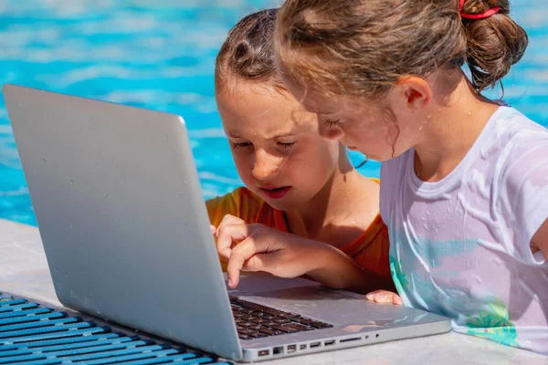 Learning always and everywhere concept. Two cute young girls learning remotely with laptop in swimming pool.