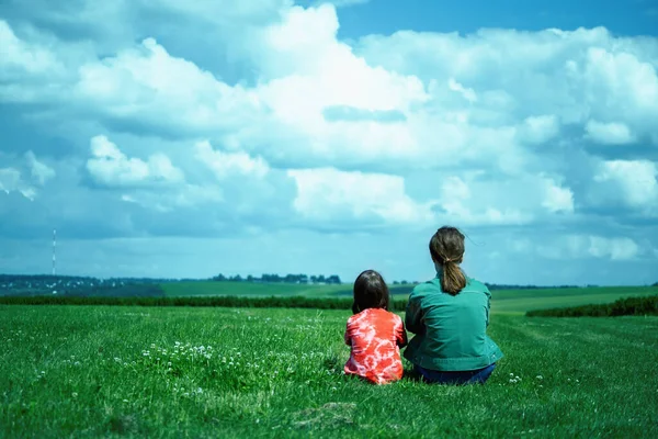 İki genç kız çimlerin üzerinde oturuyor ve uzaklığa bakıyor. Doğa, mutluluk ve sağlıklı yaşam tarzı kavramı.