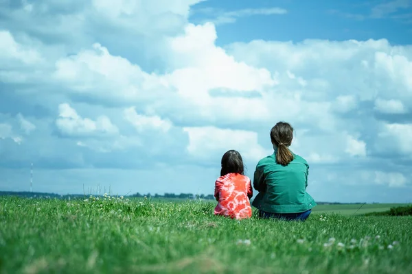 Two young girls sitting on the field of grass. Nature, happiness and healthy lifestyle concept. Horizontal image.