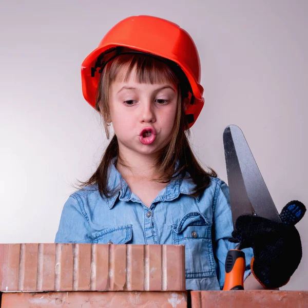 Şirin küçük inşaatçının komik görüntüsü tuğla bir duvar örüyor. İnşaat ve onarım hizmetleri kavramı.