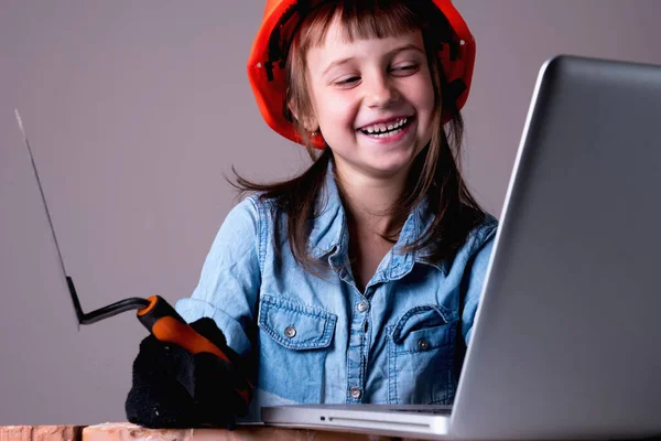 Humorous image of cute young builder with laptop builds a brick wall. Building and repair services concept. Horizontal image.
