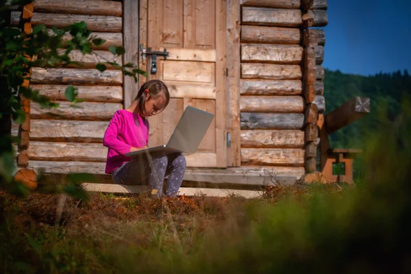 Learning always and everywhere. Young beautiful child girl uses a laptop and studies remotely outdoorson.