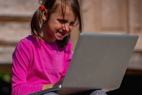 Conceptual photography: Learn always and everywhere. Portrait of young beautiful school girl uses a laptop and studies remotely outdoorson.