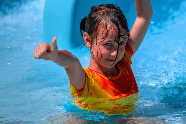 小女孩在水上公园滑行时举起手来 竖起大拇指 暑期水上公园度假快乐童年的概念 横向图像 — 图库照片