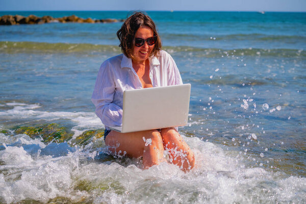 Beautiful happy business woman working remotely, using laptop computer on a beach by the sea. 