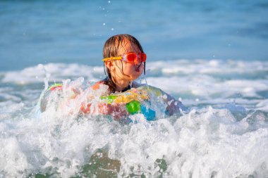 Neşeli çocuk kırılma dalgasında şişirilebilir halka sürüşünde. Seyahat, sağlıklı yaşam tarzı, yüzme aktiviteleri ve yaz tatili konsepti. Tropikal adada tatiller