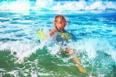 Mutlu çocuk sahilde sörf yaparken eğleniyor. Neşeli çocuk kırılma dalgasında şişirilebilir halka sürüşünde. Seyahat, sağlıklı yaşam tarzı, yüzme aktiviteleri ve yaz tatili konsepti. Tropikal adada tatiller