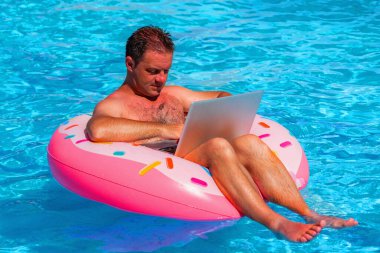 Yüzme havuzunda şişme bir dairede oturan ve bilgisayarla uzaktan çalışan bir iş adamı.. 