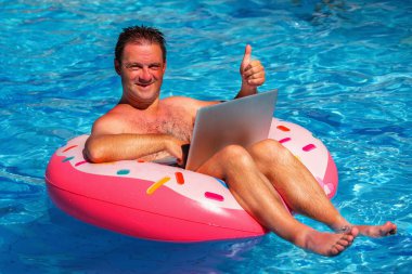 Yaz tatilinde havuzda şişirilebilir bir çemberde çalışan bir iş adamı dizüstü bilgisayarla uzaktan çalışır. Yatay resim.