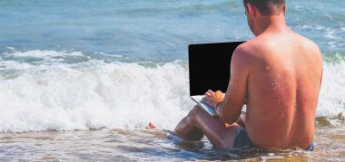 Adanın renkli sahillerinde dizüstü bilgisayarlı bir iş adamı portresi. Yaz tatili, tatil ve uzaktan çalışma konsepti. Yatay görüntü. Boşluğu kopyala.