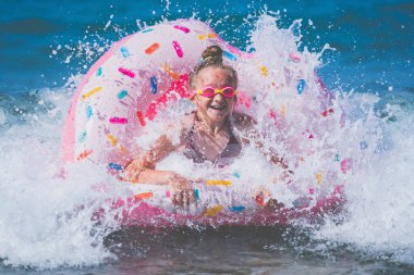Egzotik denizde yüzen şişme yüzüklü çok mutlu bir genç kız. Sahilde deniz sörfü yaparken eğleniyor. Neşeli çocuk kırılma dalgasında şişirilebilir halka gezisinde. 