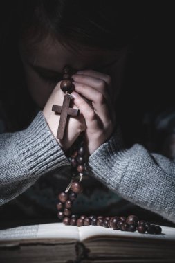 Tanrı 'ya dua et. Genç bir kızın portresi tespihle dua edip İncil okuyor. Dikey resim.