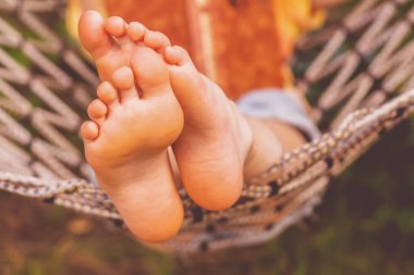 A young beautiful girl lies in a hammock. Rest, summer vacation, leisure time concept. Selective focus on feets.