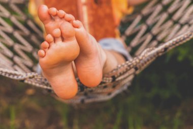A young beautiful girl lies in a hammock and reads a book.  Selective focus on feets. Horizontal image.