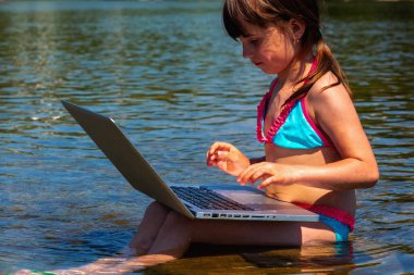 Nehir taşının üzerinde oturan ve dizüstü bilgisayar kullanan küçük tatlı bir kızın portresi.. 