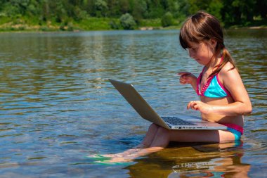 Nehir taşının üzerinde dizüstü bilgisayar kullanan tatlı bir kız çocuğu. Metin veya tasarım için boşluk kopyala. Yatay resim.