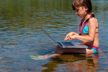 Nehir taşının üzerinde dizüstü bilgisayar kullanan tatlı bir kız çocuğu. Metin veya tasarım için boşluk kopyala.