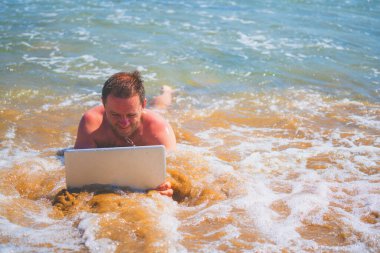 Mature businessman lying in the sea water and working with laptop. Copy space for design or text. Horizontal image. 