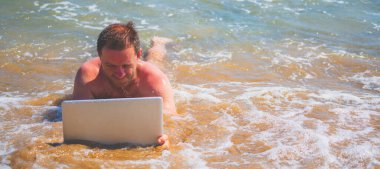 Olgun iş adamı deniz suyunda yatar ve dizüstü bilgisayarla çalışır. Tasarım veya metin için boşluk kopyala.