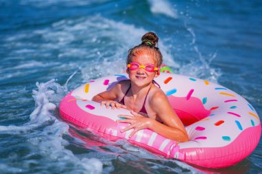 Şişme yüzüklü neşeli çocuk dalgaların üzerinde gidiyor. Seyahat, sağlıklı yaşam tarzı ve yaz tatili konsepti. Metin için alanı kopyala.