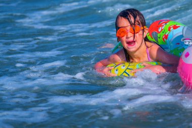 Mutlu çocuk deniz sörfünde eğleniyor. Şişme yüzüklü neşeli çocuk dalgaların üzerinde gidiyor. Seyahat, sağlıklı yaşam tarzı ve yaz tatili konsepti. Metin için alanı kopyala.