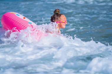 Mutlu çocuk deniz sörfünde eğleniyor. Şişme yüzükler takan neşeli çocuk dalgalara biniyor. Seyahat, sağlıklı yaşam tarzı ve yaz tatili konsepti. Boşluğu kopyala.