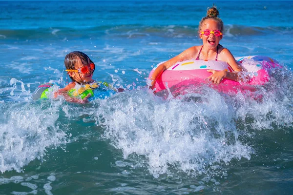 Joyful childs on inflatable rings riding on breaking wave. Travel, healthy lifestyle, swimming and summer holiday concept.