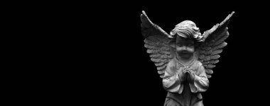 Ancient statue of little guardian angel against dark background. Black and white image. Copy space.
