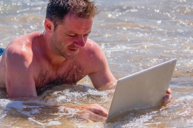 Conceptual image: education and work always and everywhere as the best way to be successful. Portrait of male entrepreneur working with laptop in the water of sea or ocean. 