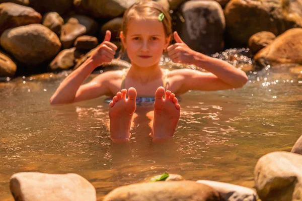 Conceptual image: autumn and winter holiday destinations to escape the cold.  Portrait of young beautiful child girl enjoy of water in lake.  Selective focus on feet.