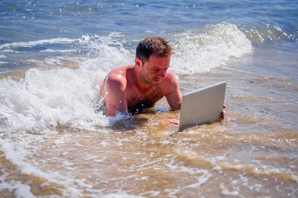 Education and work always and everywhere as the best way to be successful. Male entrepreneur working with laptop in the water of sea. Horizontal image.